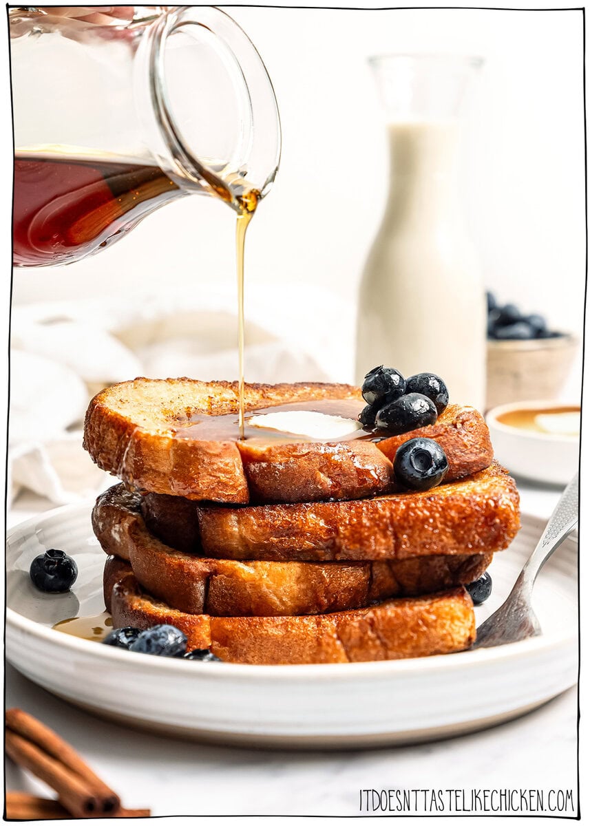 This Vegan French Toast recipe is crispy, fluffy and custardy, just like the classic! It's quick, easy and made with simple ingredients too. Pouring syrup onto stack of 4 vegan French toast slices on plate.