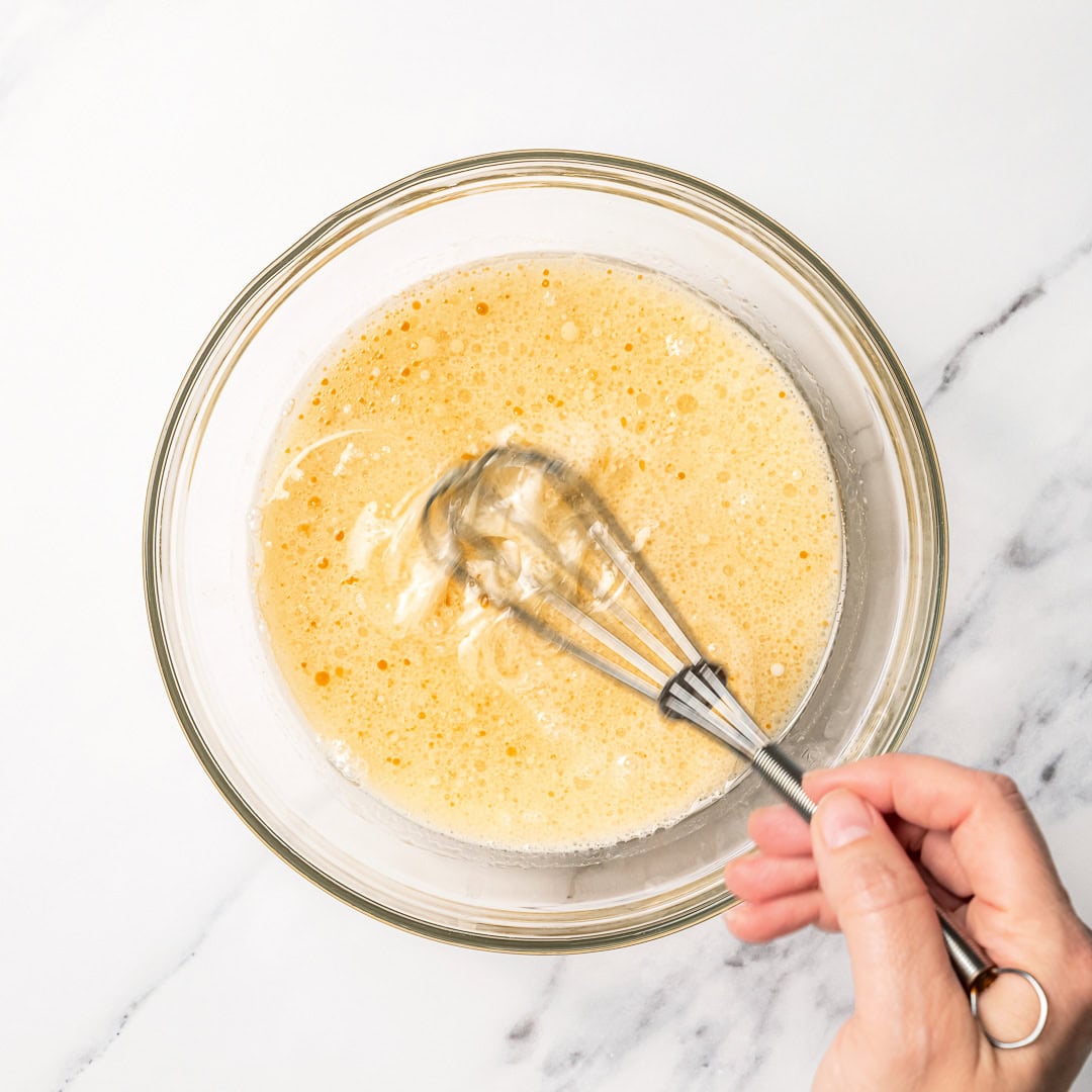 This soft and fluffy vegan vanilla cake recipe is perfect for birthdays and celebrations! It's super easy to make with pantry ingredients. Whisking wet ingredients in glass bowl.