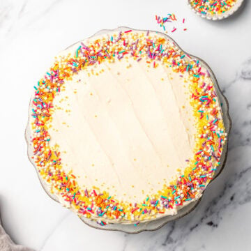 Overhead view of vegan vanilla cake on platter with sprinkles on edges.
