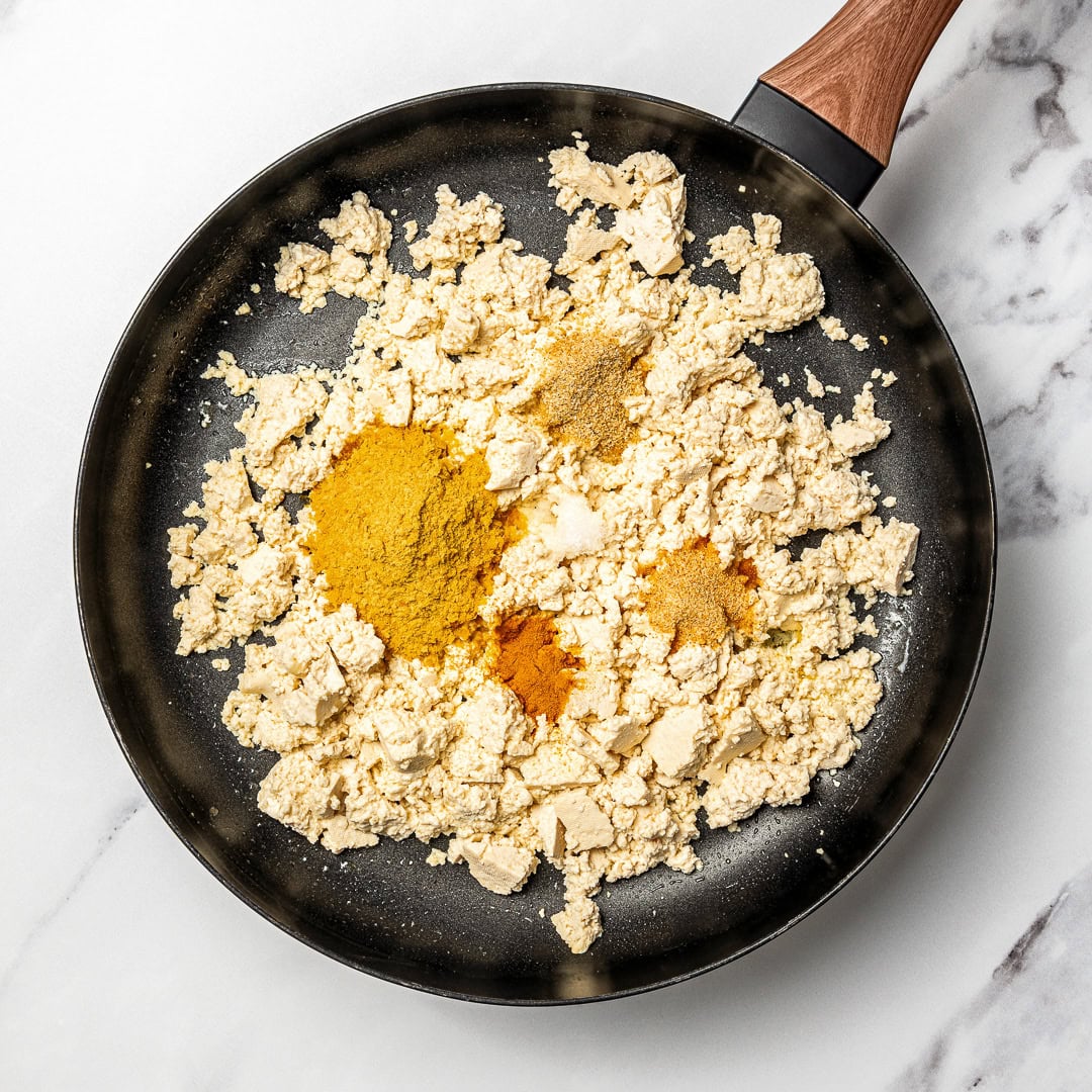Tofu scramble in a pan being cooked with spices added.