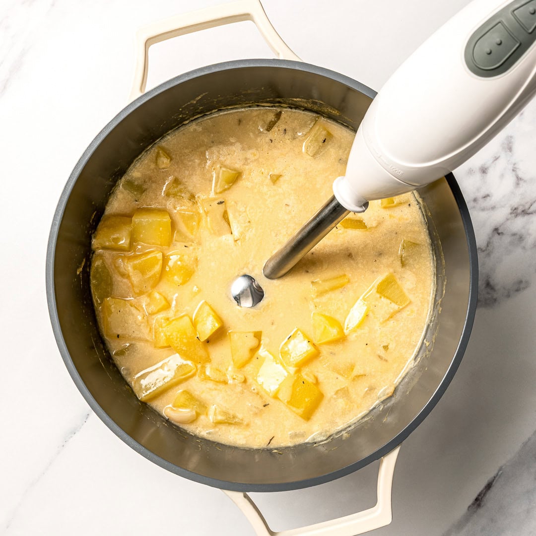 This easy creamy vegan potato soup recipe is thick, creamy, and full of cozy flavor. Think loaded baked potatoes in soup form! Immersion blender in pot of potato soup.