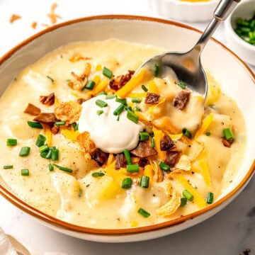 Spoon digging into bowl of creamy vegan potato soup with toppings.