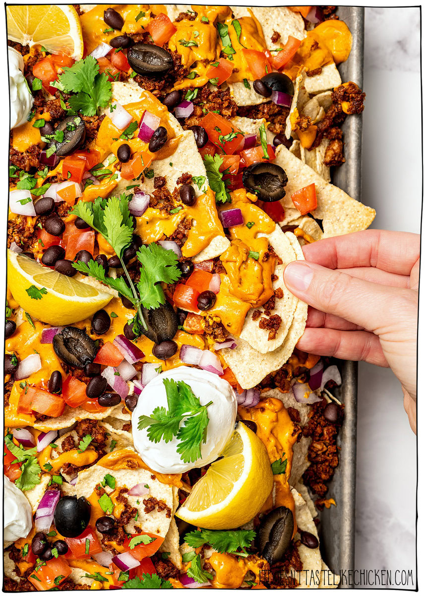 Hand lifting vegan nachos from sheet pan.
