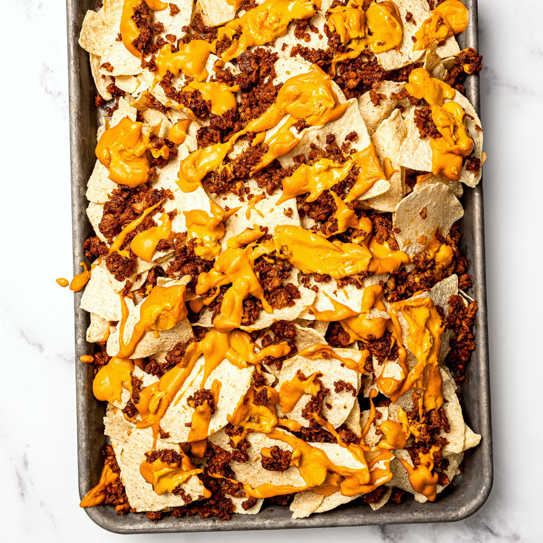 Tortilla chips on sheet pan with vegan nacho cheese sauce and taco meat.
