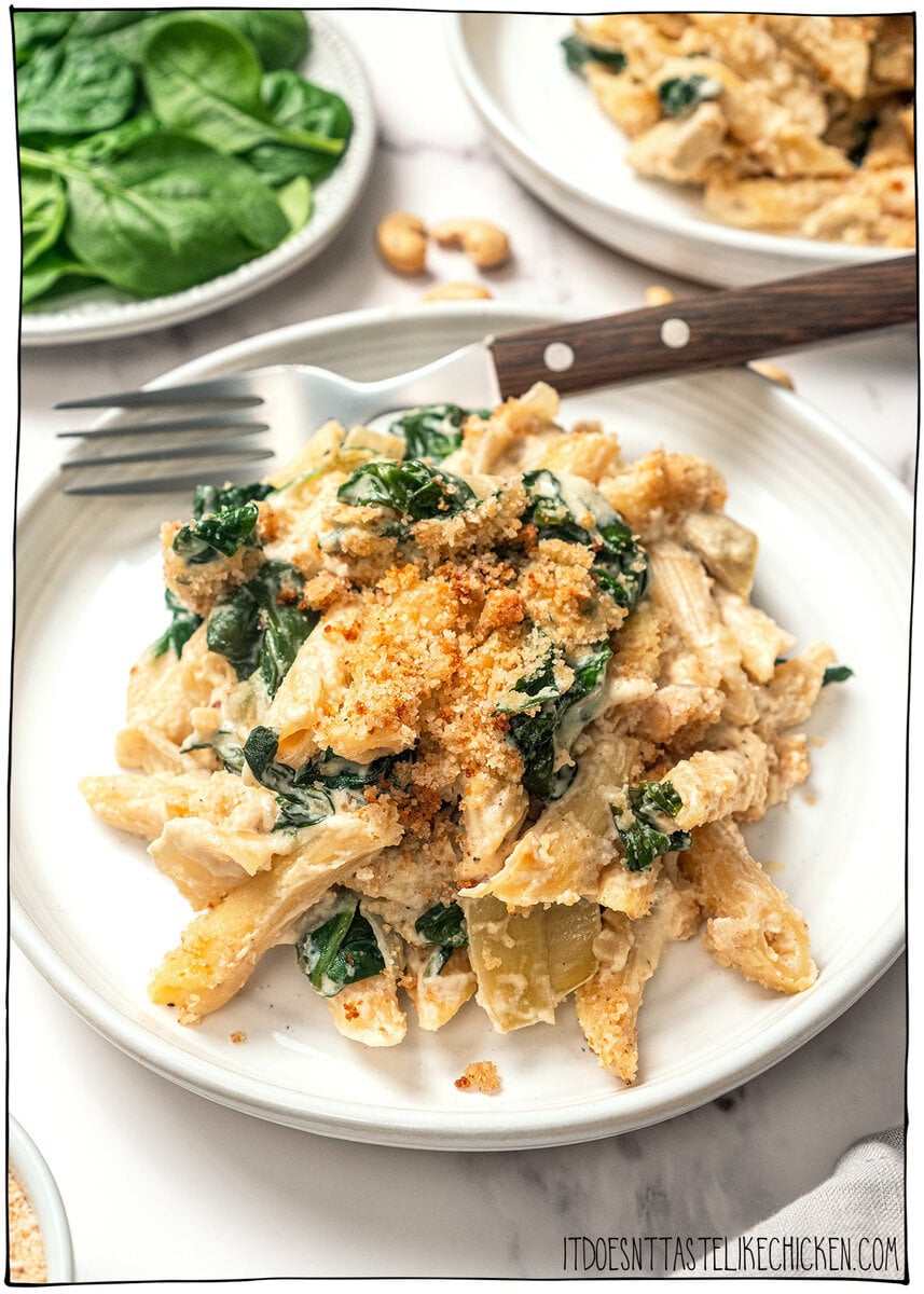 Plate of vegan spinach artichoke pasta bake with fork.
