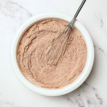 Dry ingredients for vegan chocolate cake in bowl with whisk.
