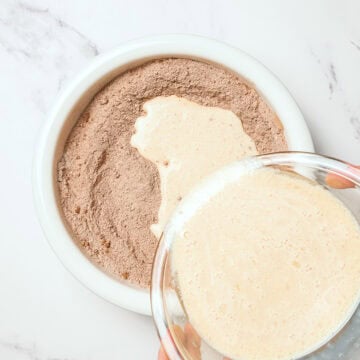 Pouring liquid ingredients into dry ingredients for vegan chocolate cake.