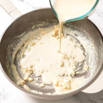 Pouring vegan milk into roux in skillet.