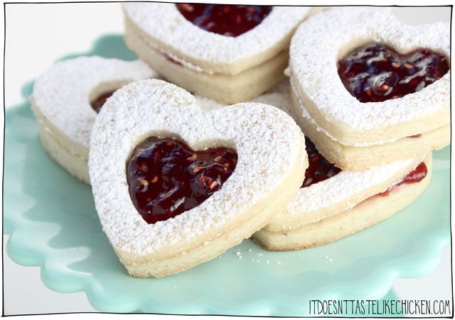 Vegan Linzer Heart Cookies! The buttery soft sugar cookie, sprinkled with powdered sugar, filled with sweet raspberry jam. They are every bit as tasty as they are adorable. Perfect for a gift for a loved one on Valentine's day or other special occasions. Egg-free, dairy-free. #itdoesnttastelikechicken #valentinesday #veganvalentines #veganbaking