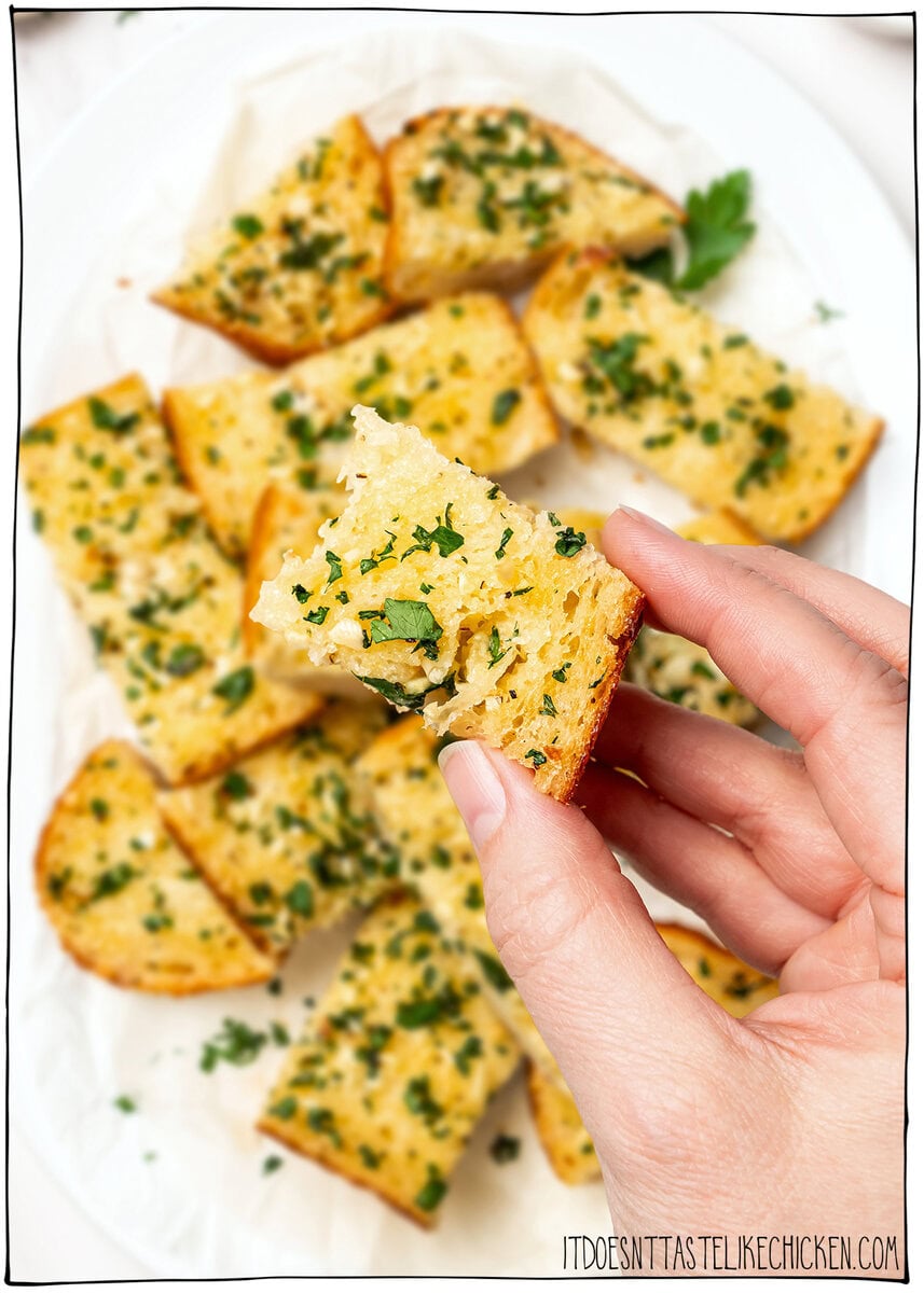 Hand holding piece of vegan garlic bread.