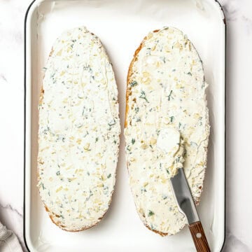 Spreading garlic butter onto bread in pan.