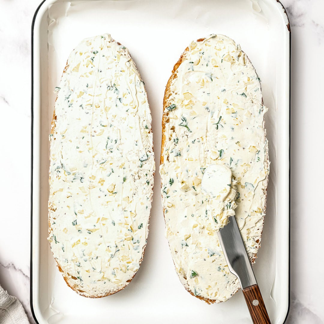 Spreading garlic butter onto bread in pan.