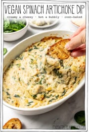 Crostini dipping into baking dish with text overlay that reads vegan spinach artichoke dip.