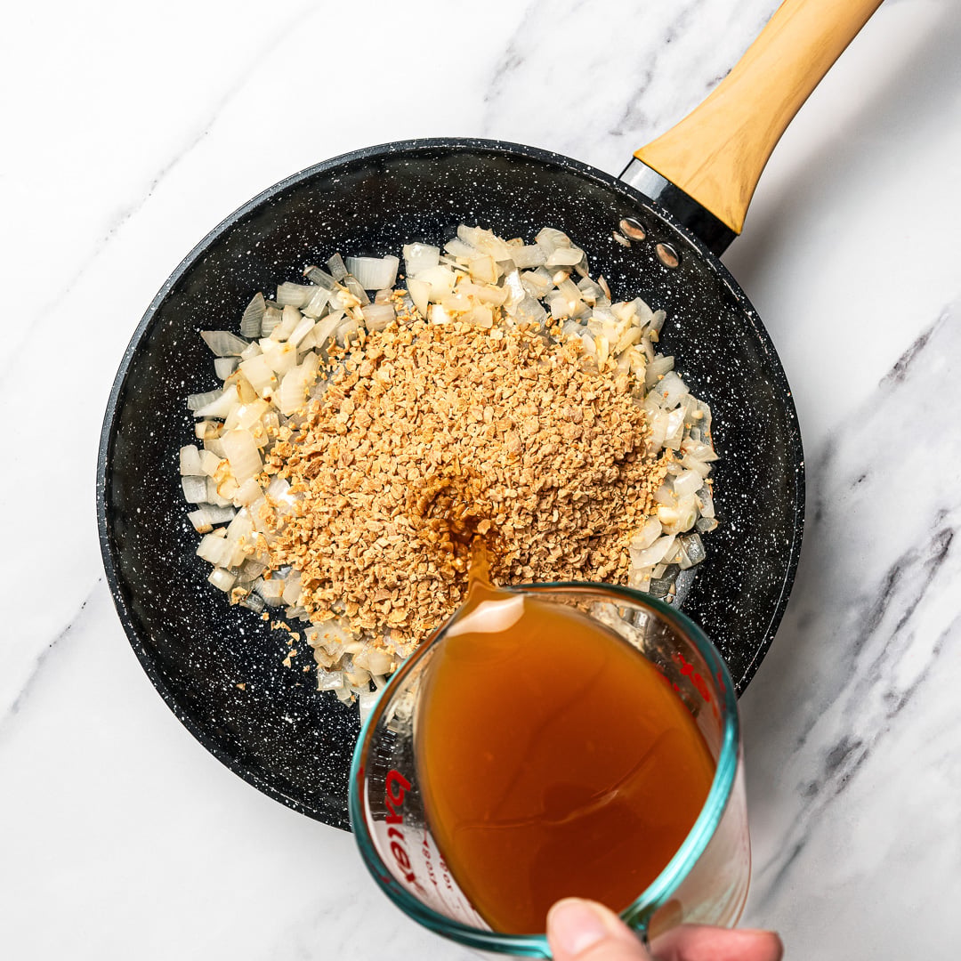 Pouring broth into pan with TVP, onions, and garlic.