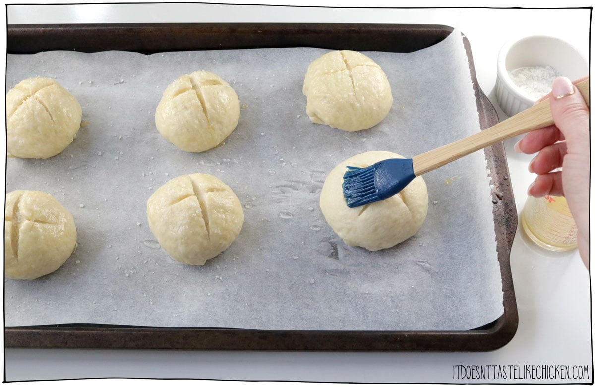 Score the buns, brush with vegan butter, and sprinkle with salt, then bake,