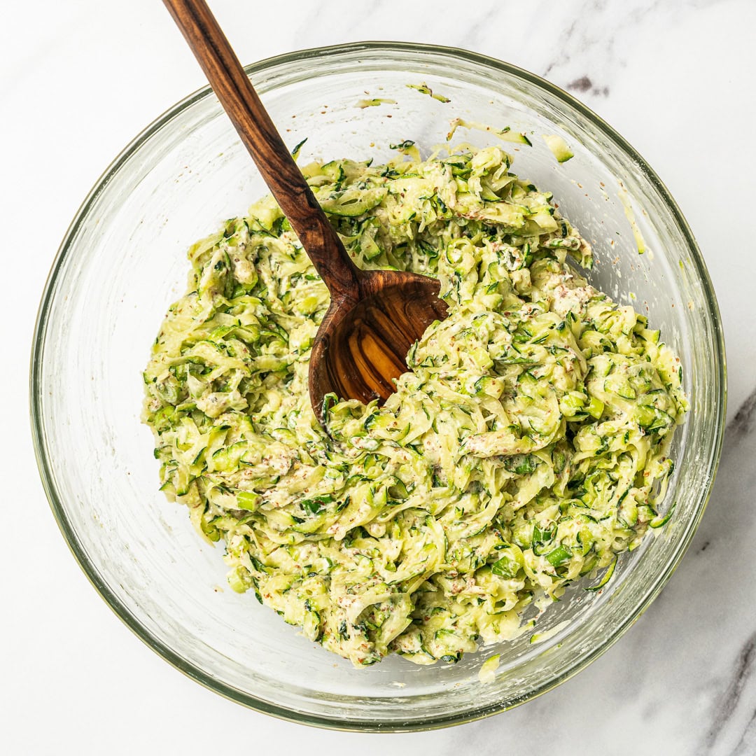Stirring zucchini fritter mixture in bowl.