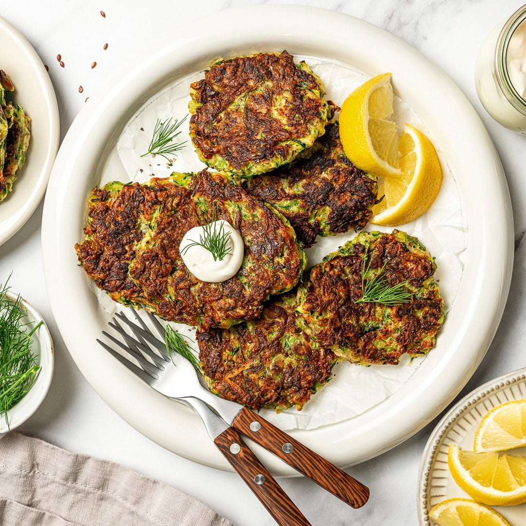 Plate of zucchini fritters with lemon wedges.