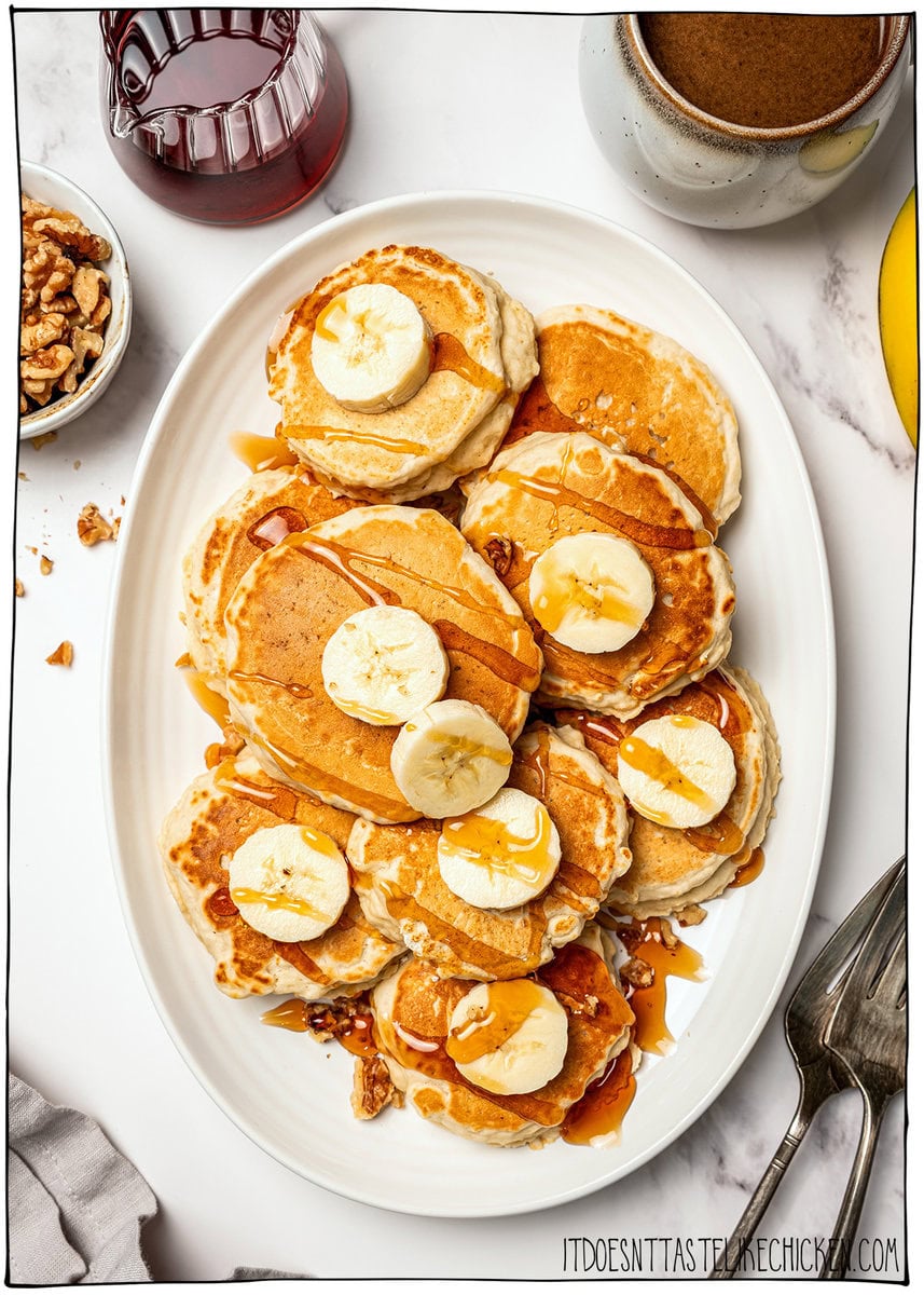 Banana oat pancakes on platter with syrup, banana slices, and walnuts.
