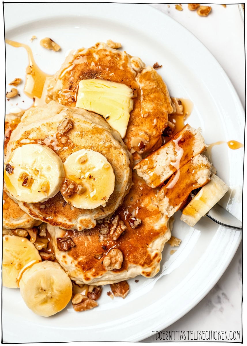 Banana oat pancakes topped with banana slices, walnuts, and maple syrup, with a fork holding a bite