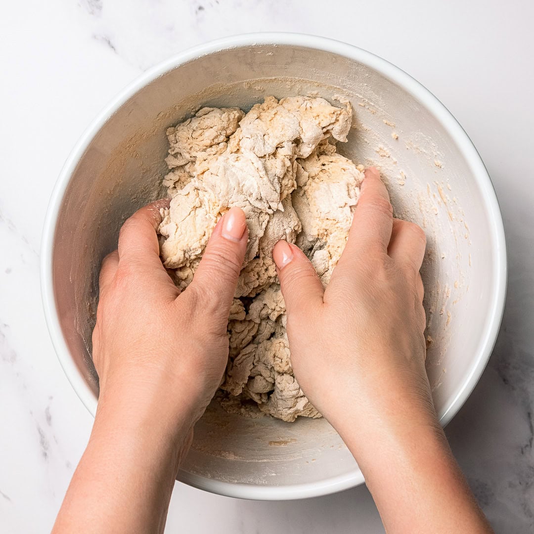 Hands mixing dough for protein bagel buns in bowl.