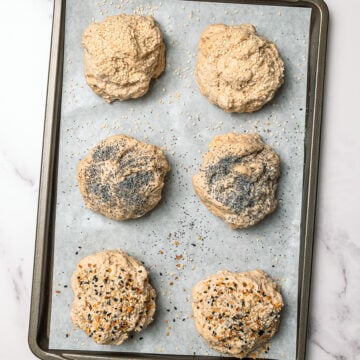 Unbaked protein bagel buns on parchment lined sheet pan.