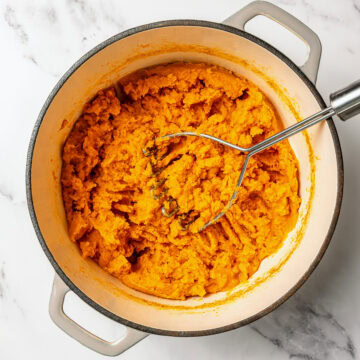 Potato masher in pot of mashed sweet potatoes.
