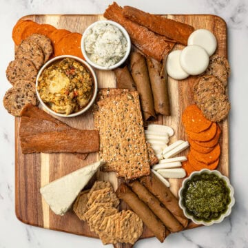 Vegan charcuterie board in progress with crackers, dips, vegan meats and cheeses.