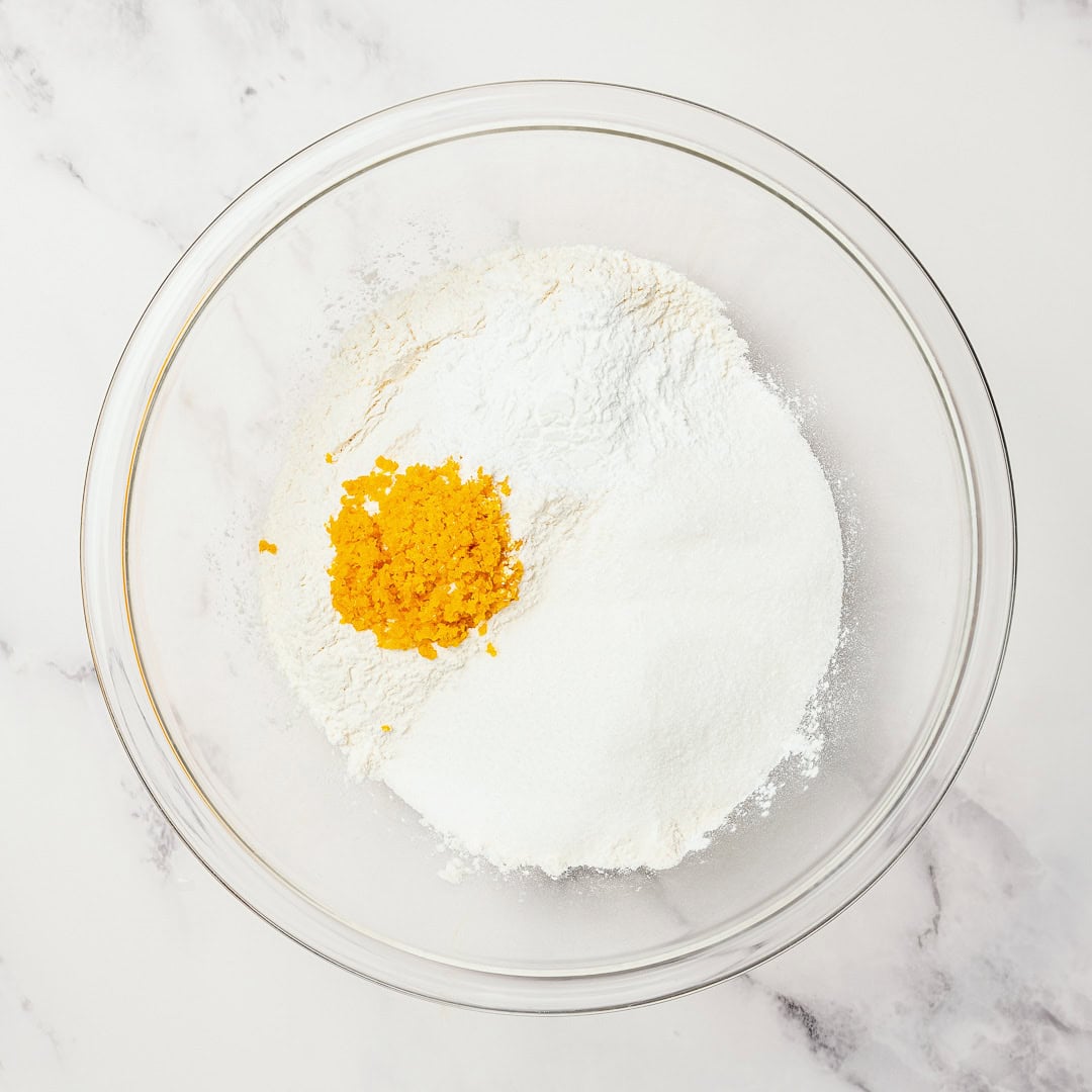 These easy Vegan Cranberry Orange Scones are flaky, citrusy, and full of festive flavor. Perfect for holiday brunches or a cozy winter treat! Dry ingredients and orange zest in glass bowl.