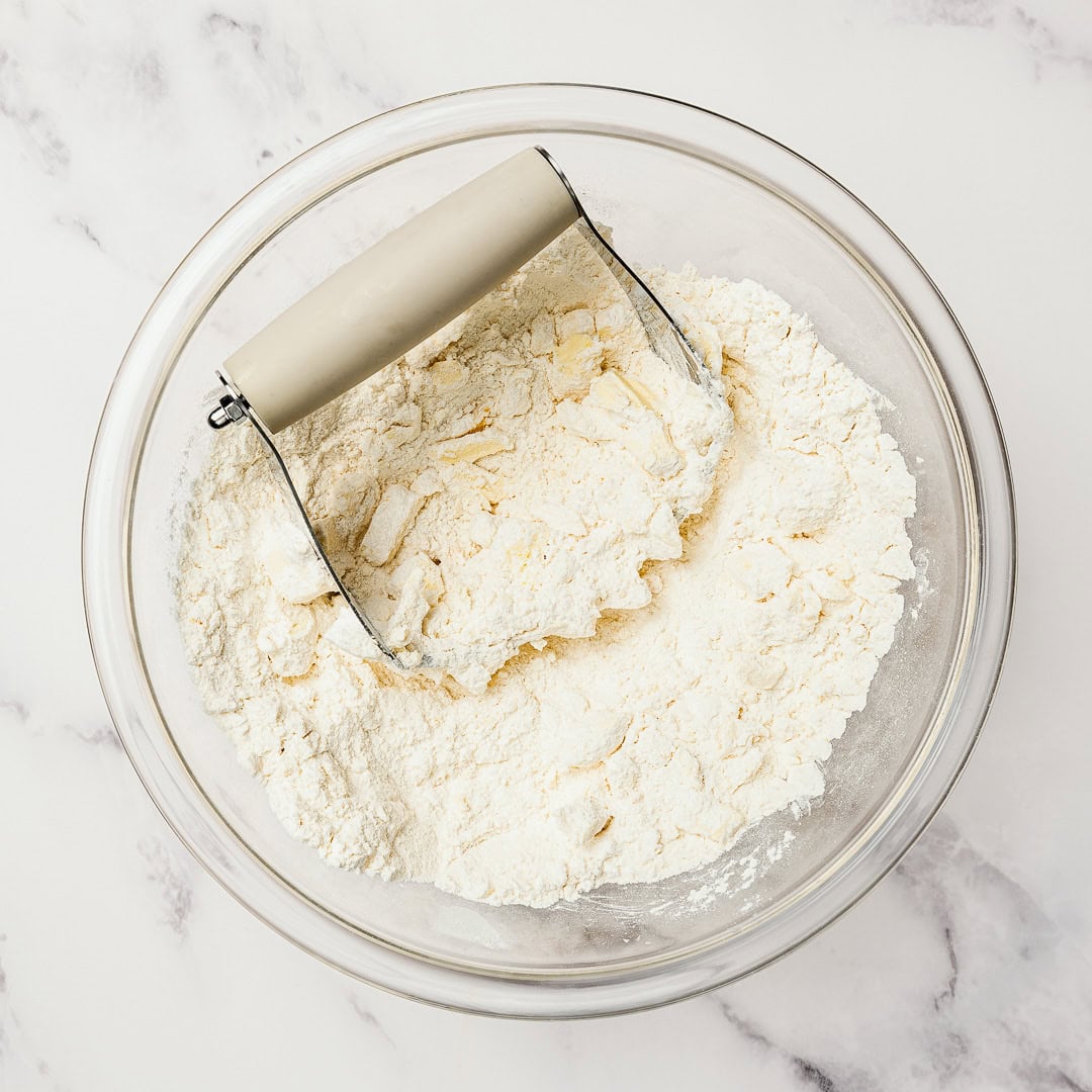 These easy Vegan Cranberry Orange Scones are flaky, citrusy, and full of festive flavor. Perfect for holiday brunches or a cozy winter treat! Pastry cutter in bowl with dry ingredients and butter.