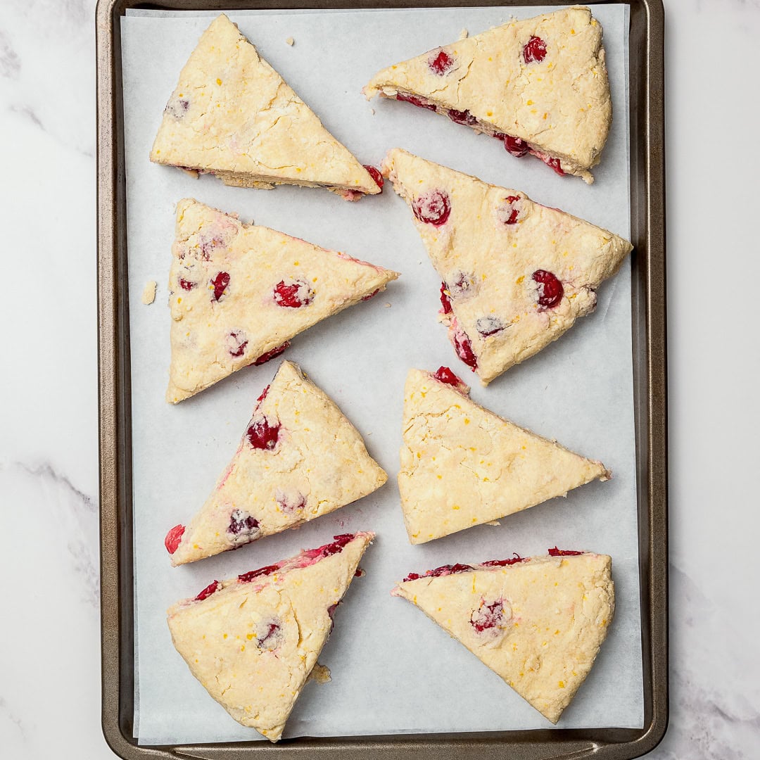 These easy Vegan Cranberry Orange Scones are flaky, citrusy, and full of festive flavor. Perfect for holiday brunches or a cozy winter treat! Unbaked cranberry orange scones on parchment lined baking sheet.