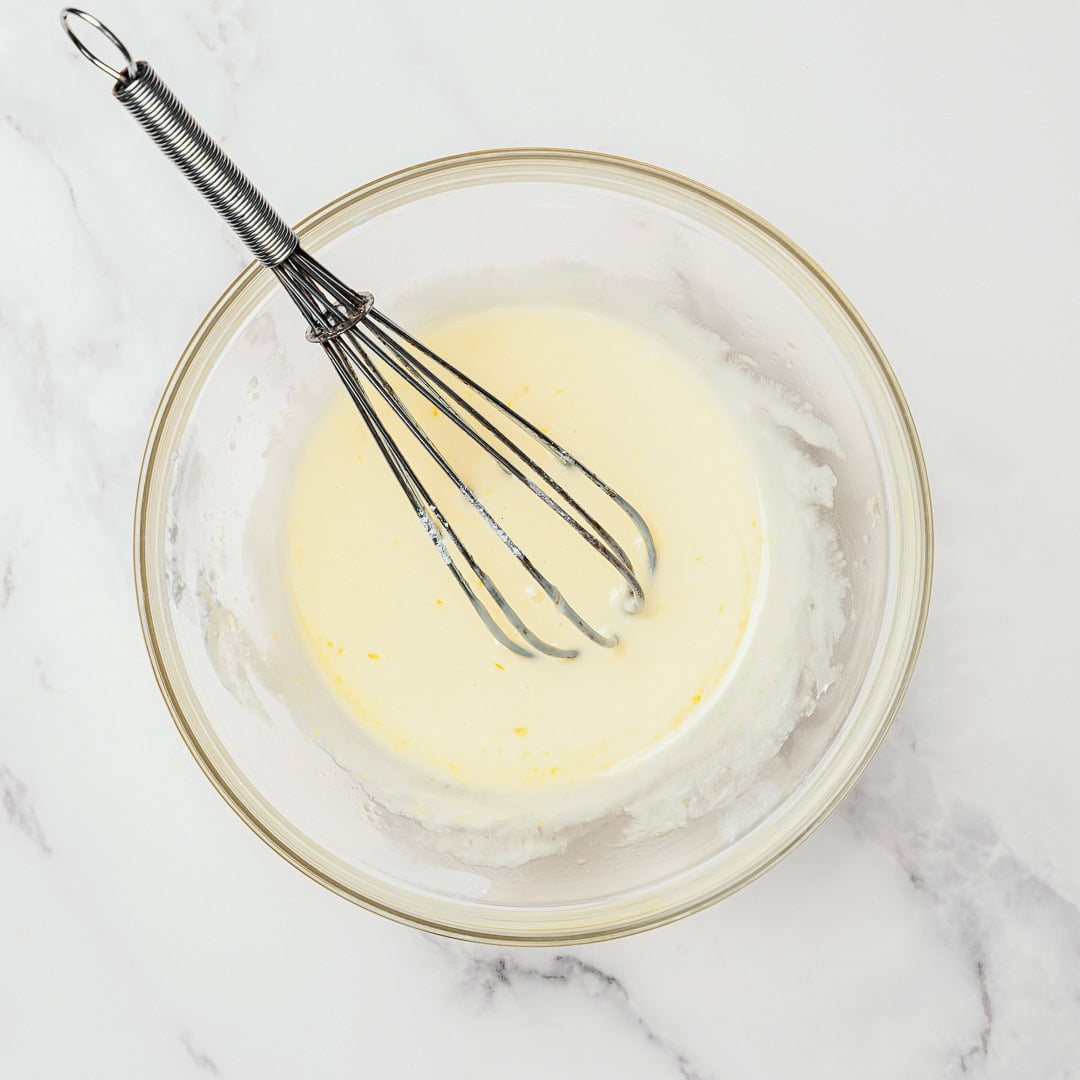These easy Vegan Cranberry Orange Scones are flaky, citrusy, and full of festive flavor. Perfect for holiday brunches or a cozy winter treat! Whisking glaze in glass bowl.