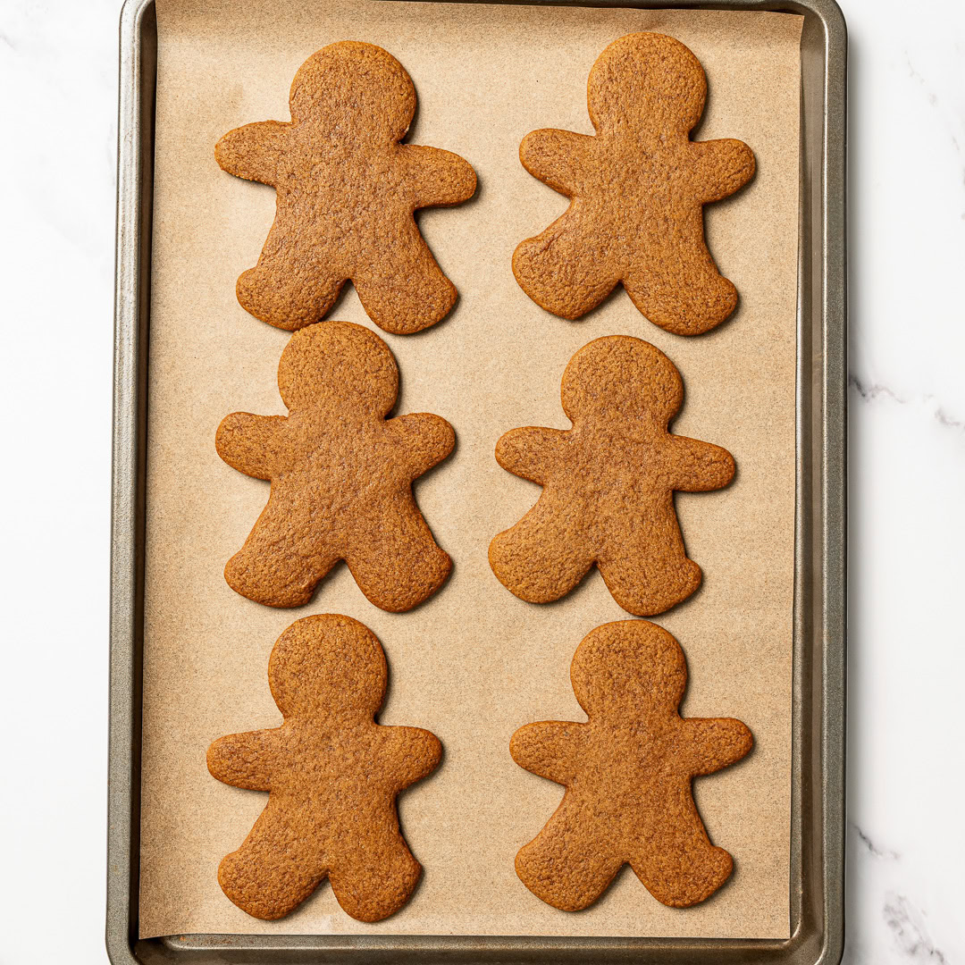 Soft, chewy and perfectly spiced, these vegan gingerbread cookies are made with rich molasses and warm spices. Easy to roll, cut and decorate! Baked vegan gingerbread man cookies on parchment-lined pan.