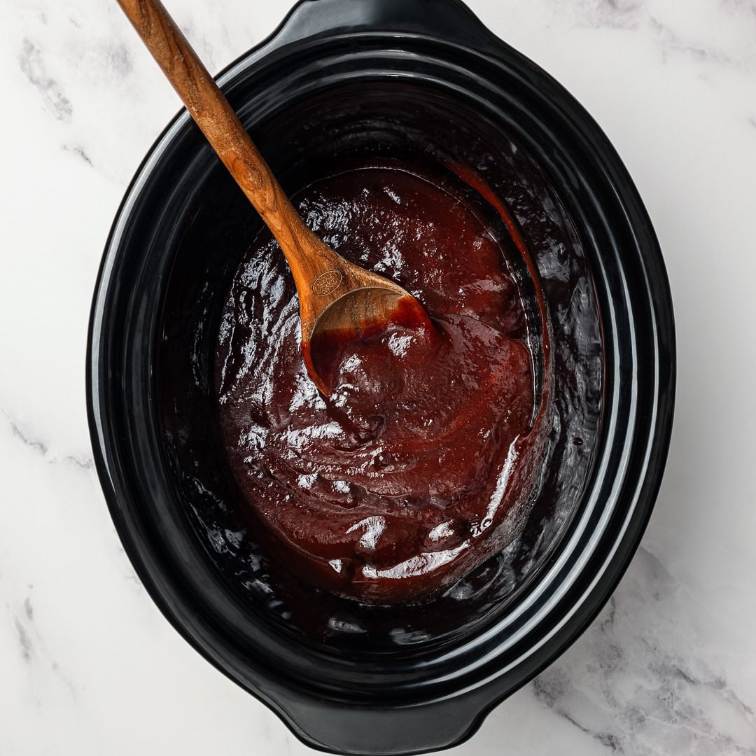 Vegan Grape Jelly Meatballs are sweet, tangy, and effortless! An easy crowd-pleasing slow cooker appetizer perfect for parties and holidays. Stirring grape jelly sauce in slow cooker.