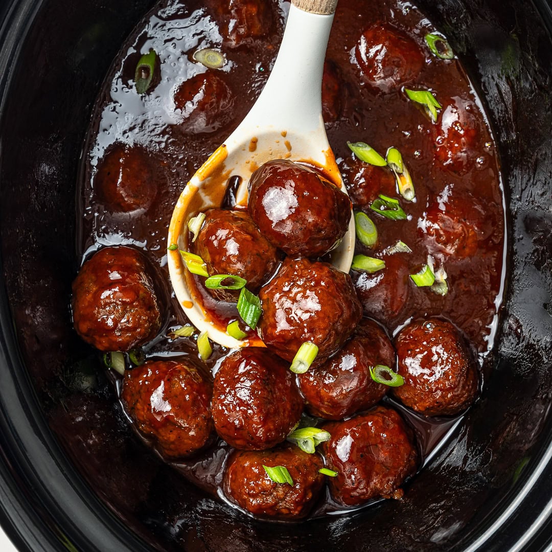 Vegan Grape Jelly Meatballs are sweet, tangy, and effortless! An easy crowd-pleasing slow cooker appetizer perfect for parties and holidays. Spoon scooping vegan grape jelly meatballs from slow cooker.