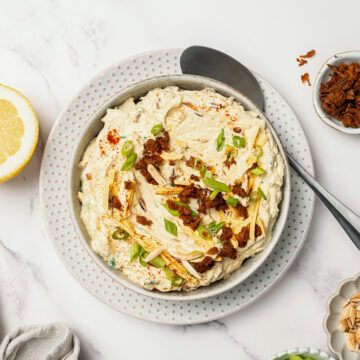 Bowl of vegan million dollar dip garnished with bacon and green onions.