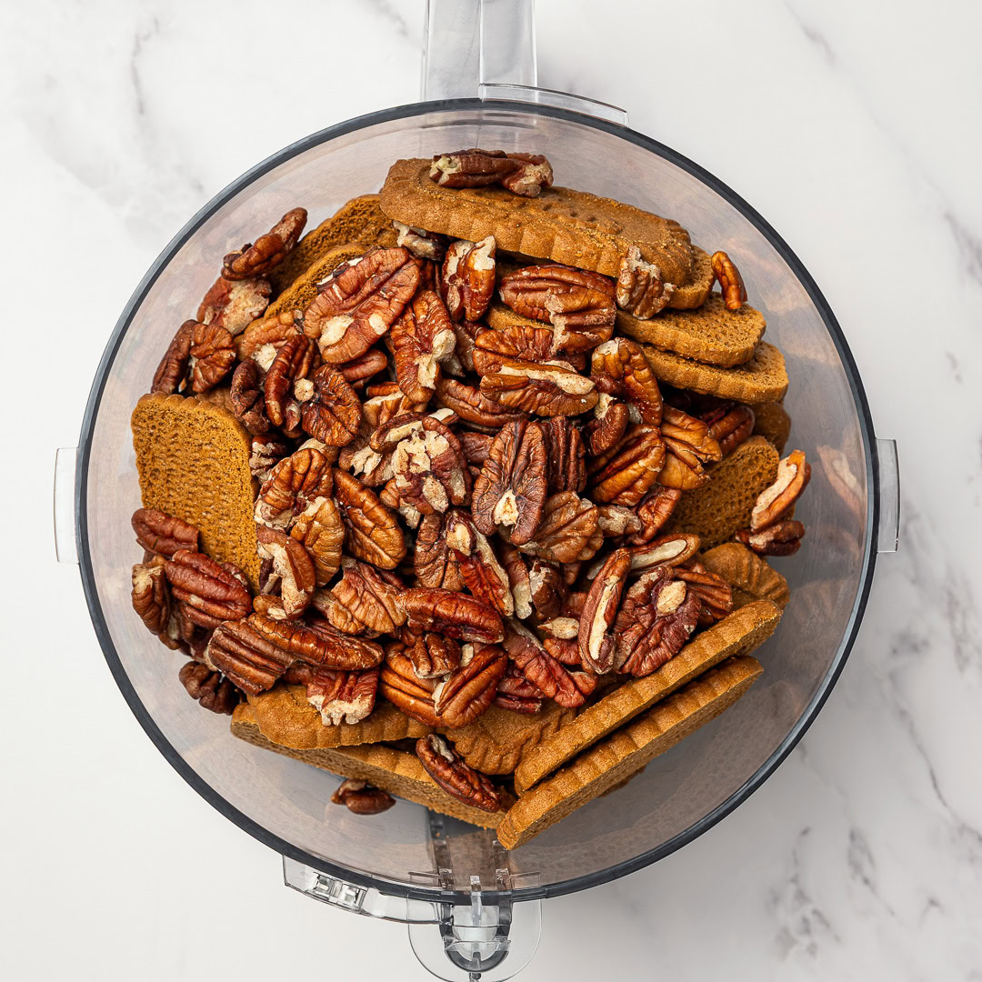 Rich, fudgy Vegan Rum Balls are an easy no-bake holiday treat! Customizable, great for gifting, and delicious with or without alcohol. Pecans and biscoff cookies in food processor bowl.