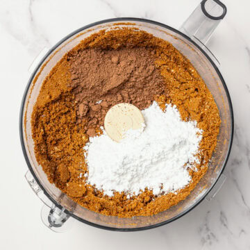 Powdered sugar added to food processor bowl with ingredients for rum balls.