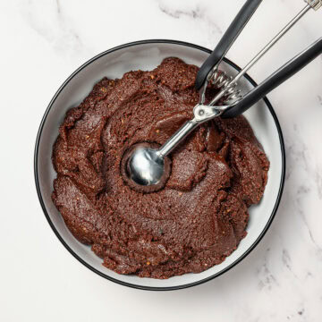 Fudgy rum ball mixture in bowl with cookie dough scoop.