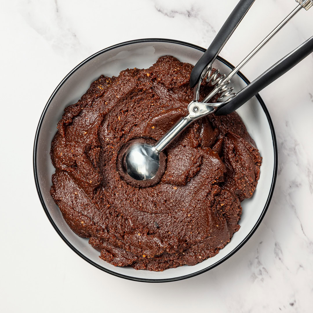 Rich, fudgy Vegan Rum Balls are an easy no-bake holiday treat! Customizable, great for gifting, and delicious with or without alcohol. Fudgy rum ball mixture in bowl with cookie dough scoop.
