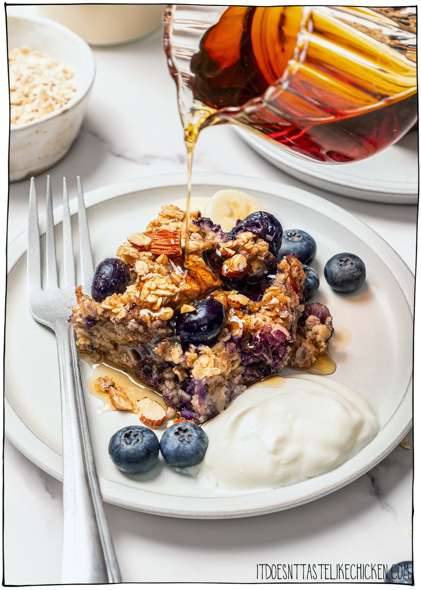 This cozy vegan baked oatmeal is easy to make, customizable, and perfect for meal prep. Mix in one bowl and enjoy any flavor combo! Pouring maple syrup onto square of baked oatmeal with blueberries.