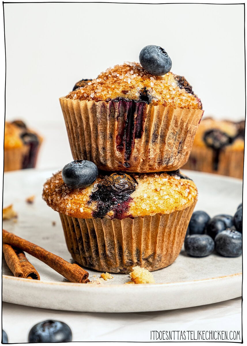 These bakery-style vegan blueberry muffins are made in one bowl, super easy! They're soft, fluffy, and finished with a crunchy sugar top. Stack of two bakery-style vegan blueberry muffins.