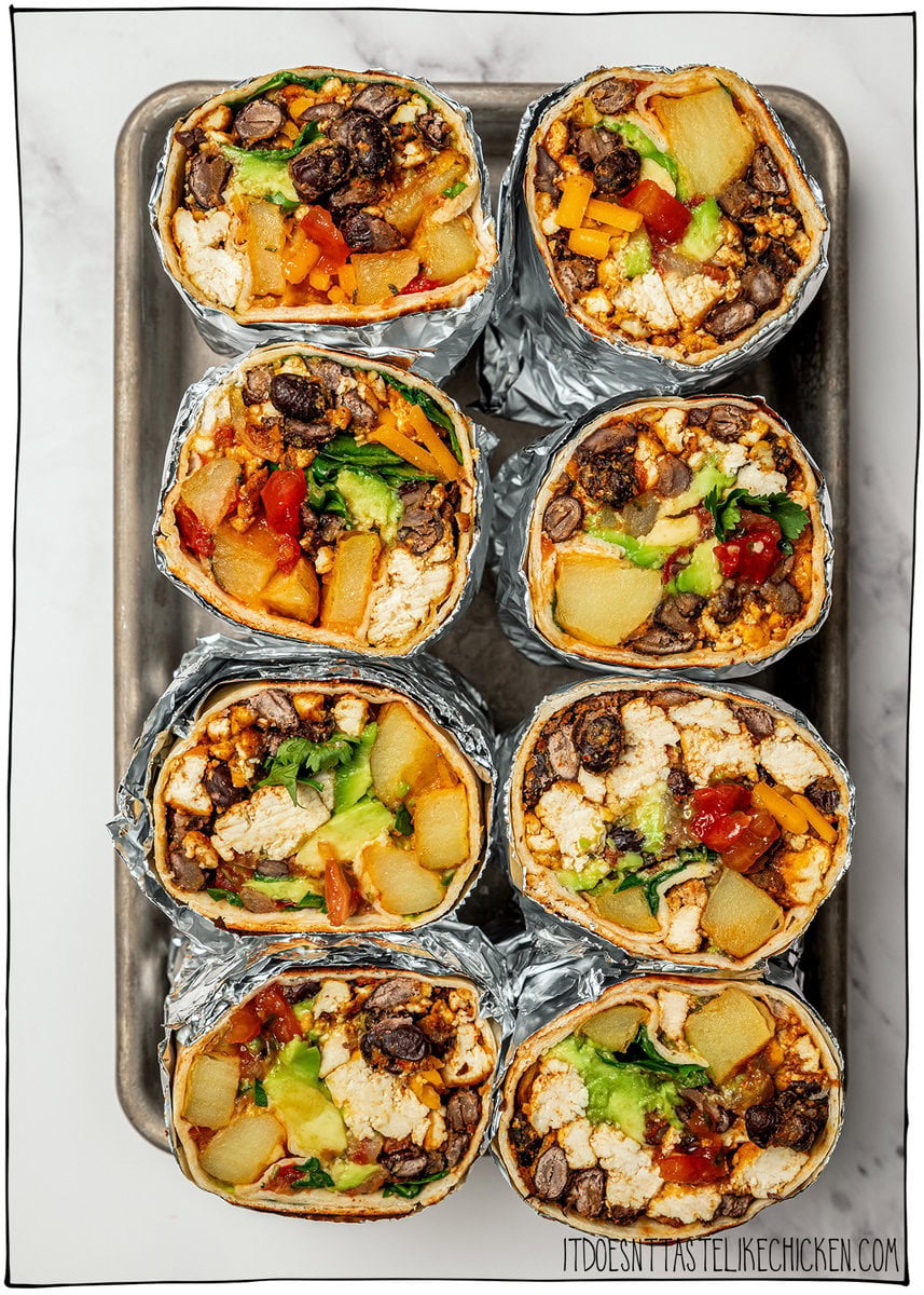 These freezer-friendly vegan breakfast burritos are packed with tofu scramble, crispy potatoes and cheese. Heat and eat for busy mornings! 8 vegan breakfast burritos standing upright in pan, sliced in half to show fillings.