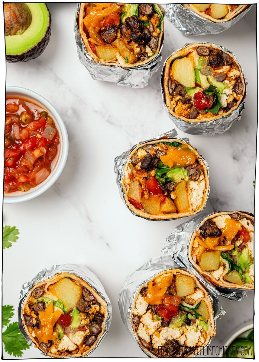These freezer-friendly vegan breakfast burritos are packed with tofu scramble, crispy potatoes and cheese. Heat and eat for busy mornings! Halved foil-wrapped vegan breakfast burritos with bowl of salsa.