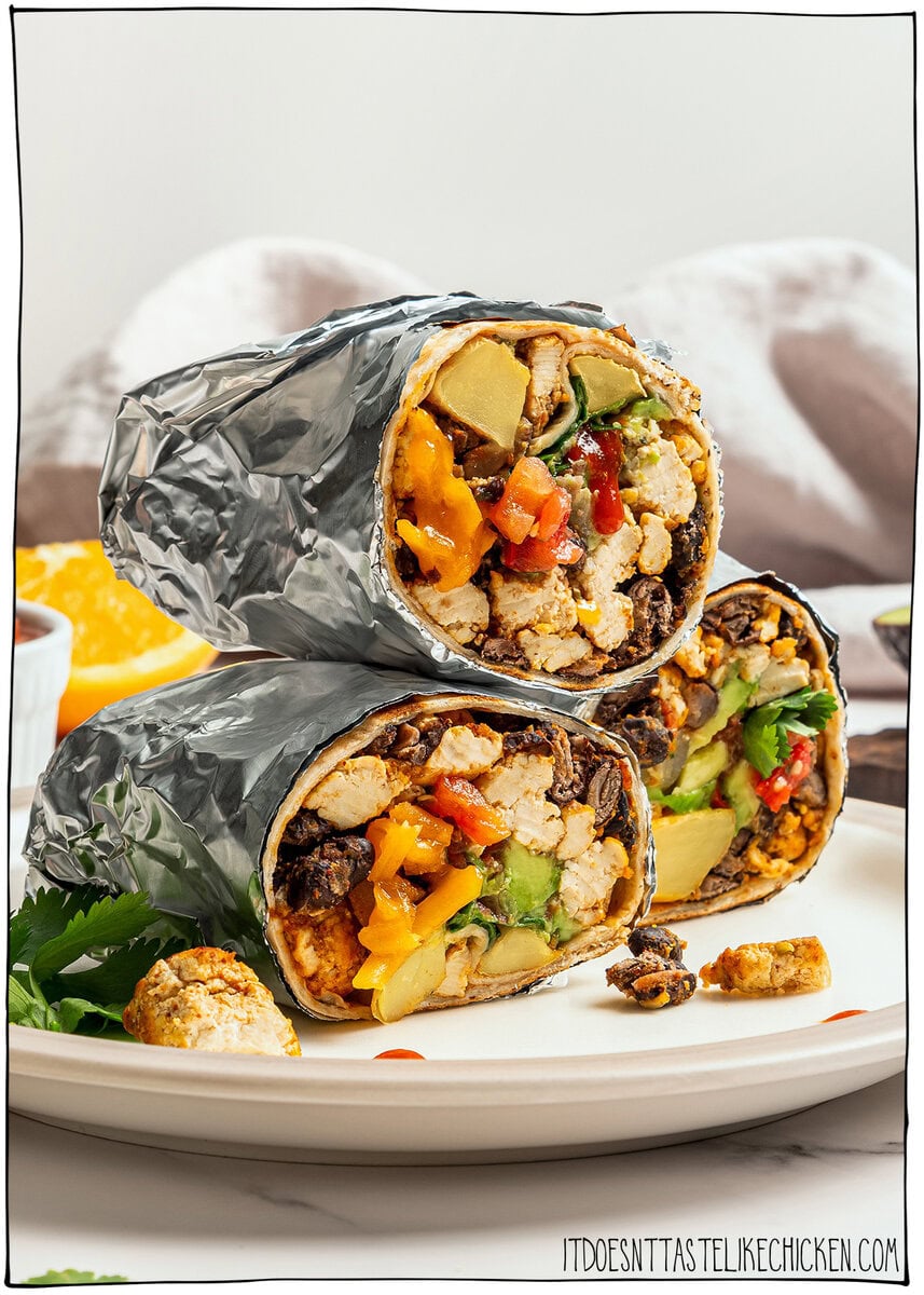 These freezer-friendly vegan breakfast burritos are packed with tofu scramble, crispy potatoes and cheese. Heat and eat for busy mornings! Stack of 3 halved vegan breakfast burritos on plate showing tofu and vegetables inside.