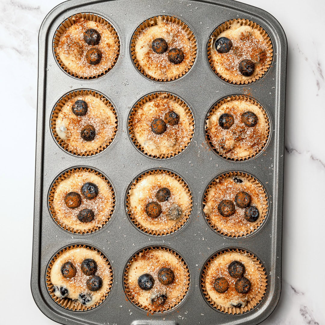 These bakery-style vegan blueberry muffins are made in one bowl, super easy! They're soft, fluffy, and finished with a crunchy sugar top. Unbaked vegan blueberry muffins in pan.