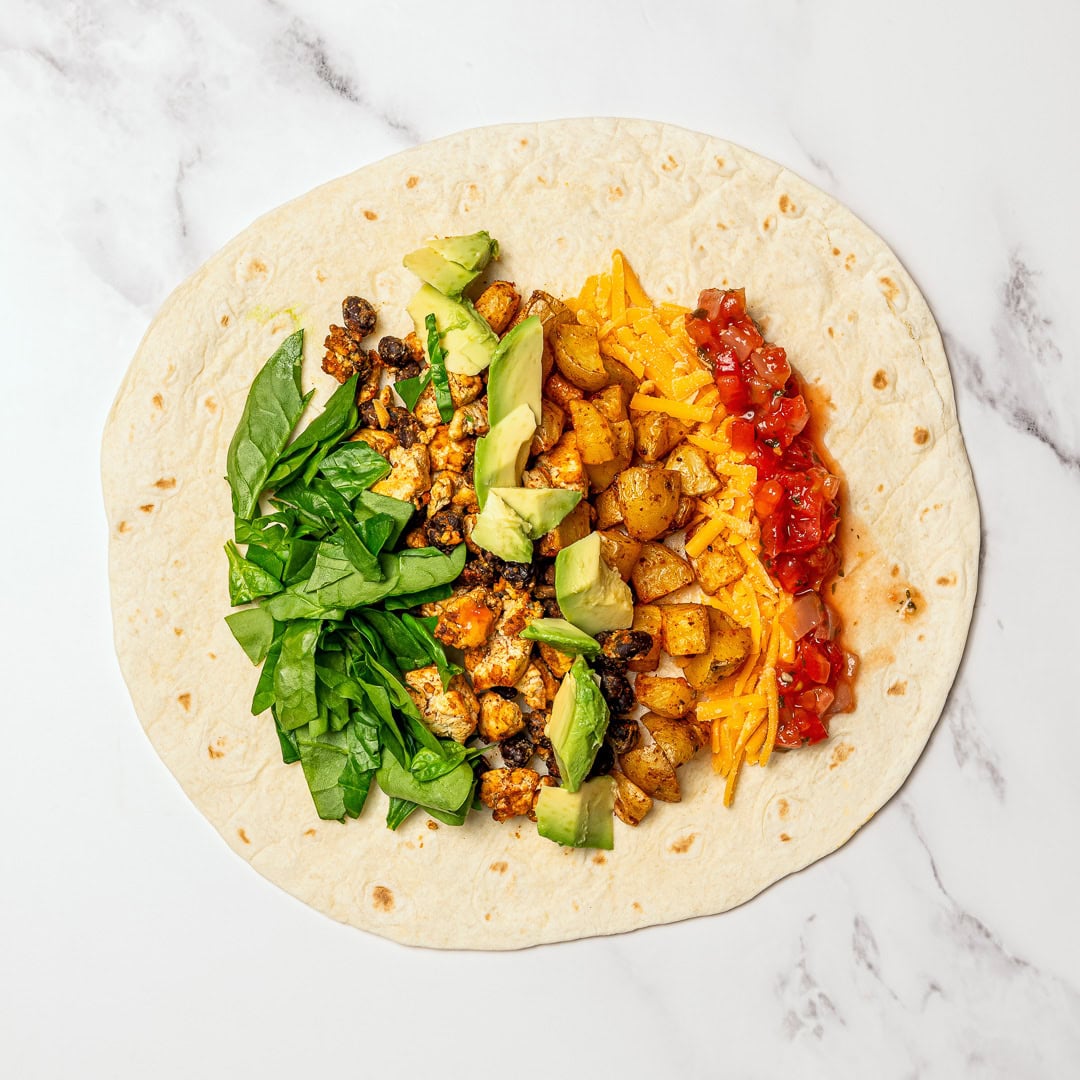 These freezer-friendly vegan breakfast burritos are packed with tofu scramble, crispy potatoes and cheese. Heat and eat for busy mornings! Vegan breakfast burrito fillings on tortilla.
