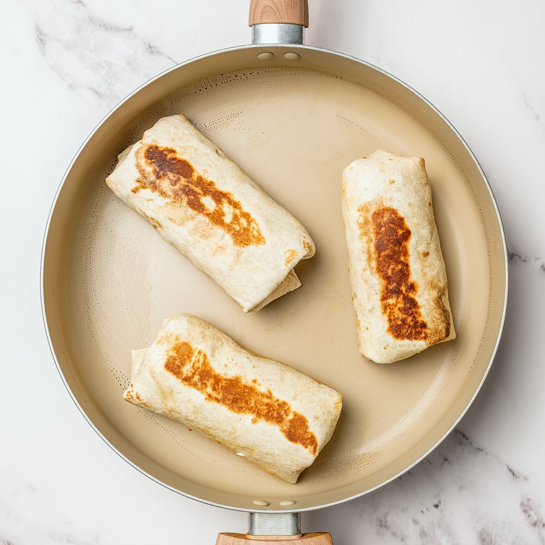 These freezer-friendly vegan breakfast burritos are packed with tofu scramble, crispy potatoes and cheese. Heat and eat for busy mornings! Toasted breakfast burritos in skillet.