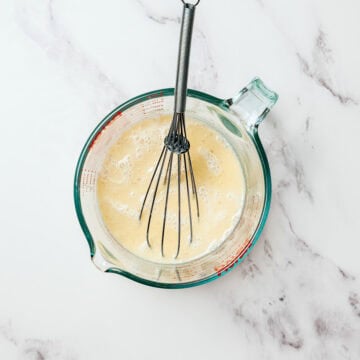 Whisk in liquid measuring cup with wet ingredients for cupcakes.