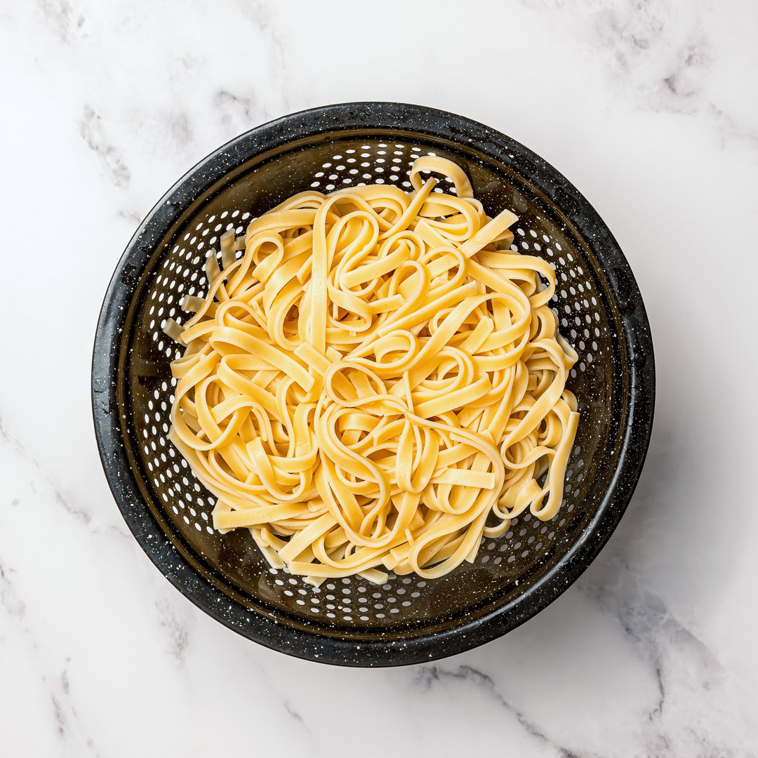 Silky and full of garlicky flavor, this creamy vegan fettuccine Alfredo is the easiest EVER because it's made without nuts or a blender! Cooked fettuccine in strainer.