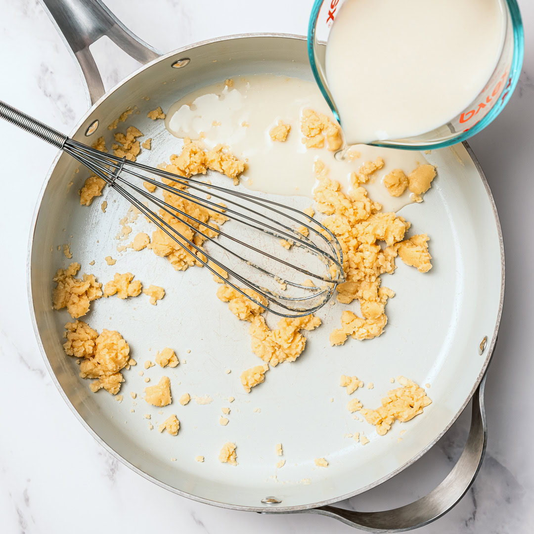 Silky and full of garlicky flavor, this creamy vegan fettuccine Alfredo is the easiest EVER because it's made without nuts or a blender! Pouring vegan milk into skillet with roux.